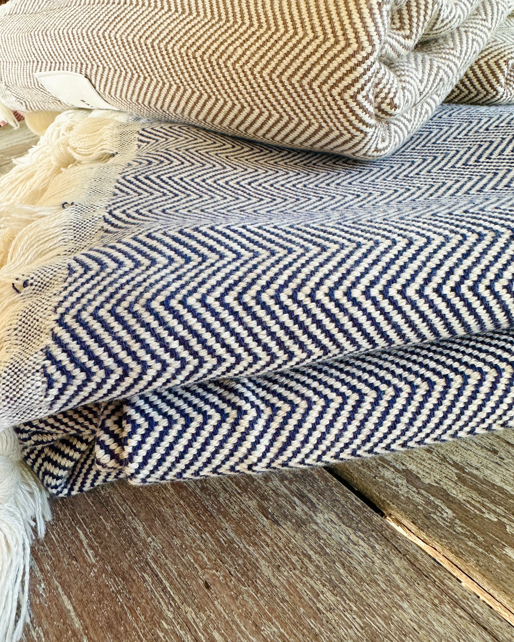 Jetés CHEVRON crème, marine et brun pliés sur une table en bois, franges nouées