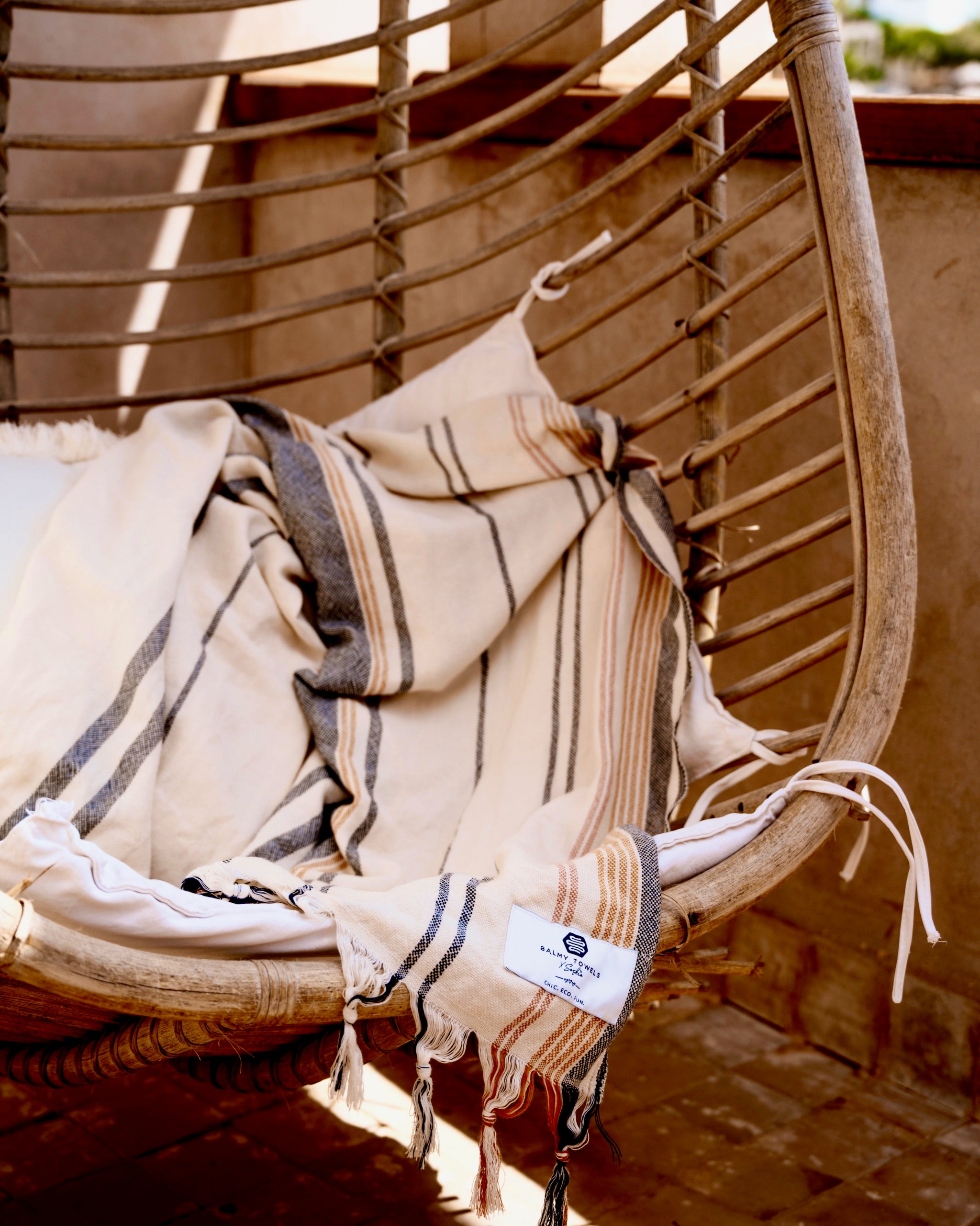 A Noa towel draped over a hanging rattan chair