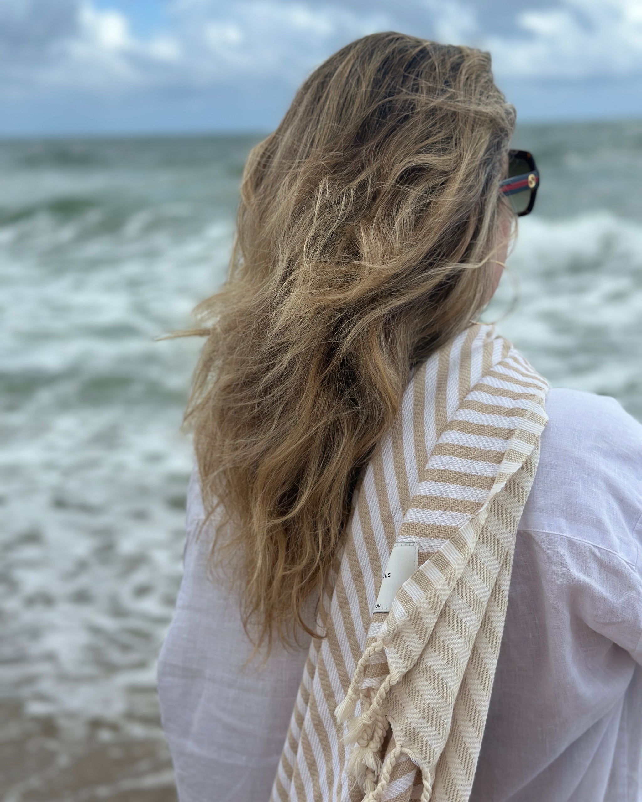 Une femme au bord de la mer avec une serviette Serena sur l'épaule