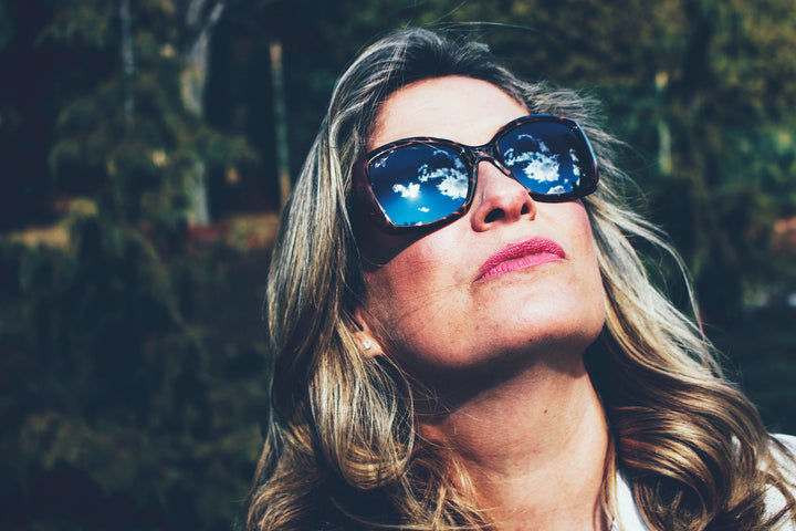 Saskia Thuot lève le visage vers le soleil, ses lunettes de soleil reflétant un ciel bleu et des nuages