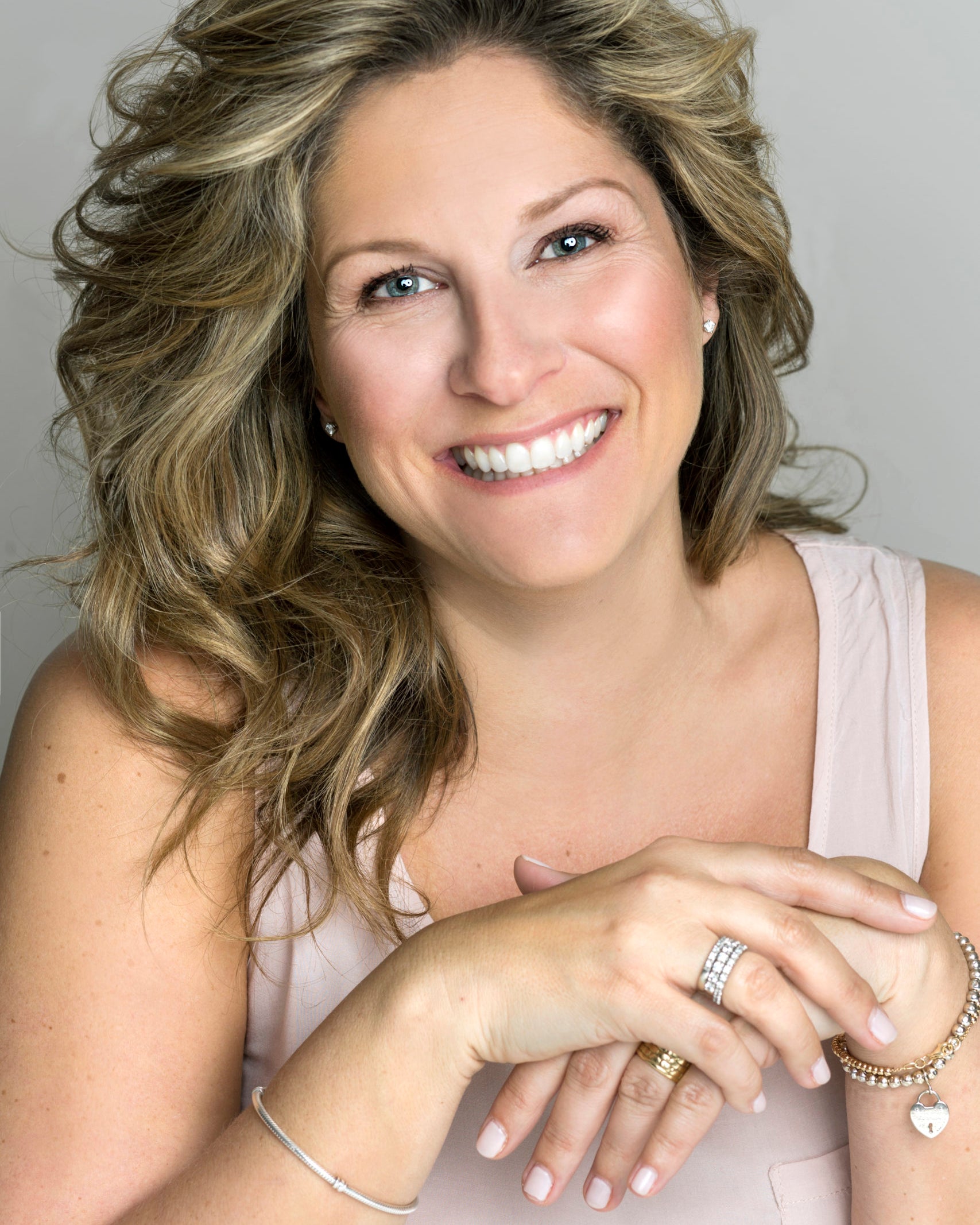 Portrait de Saskia Thuot, souriante, aux longs cheveux blonds ondulés, sur fond gris clair