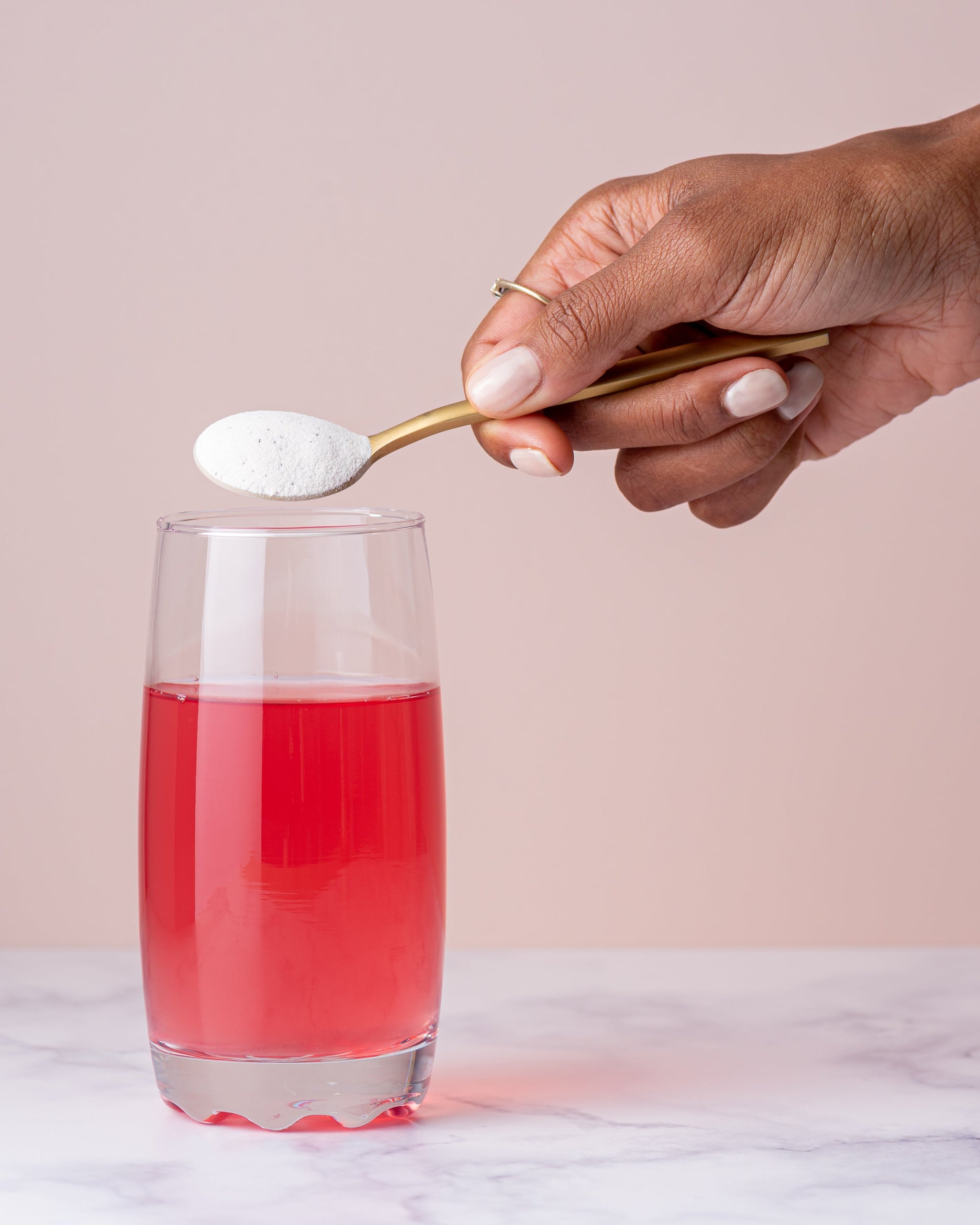 Gold spoon of Bend Beauty Marine Collagen + Co-Factors powder held above a glass of pink drink