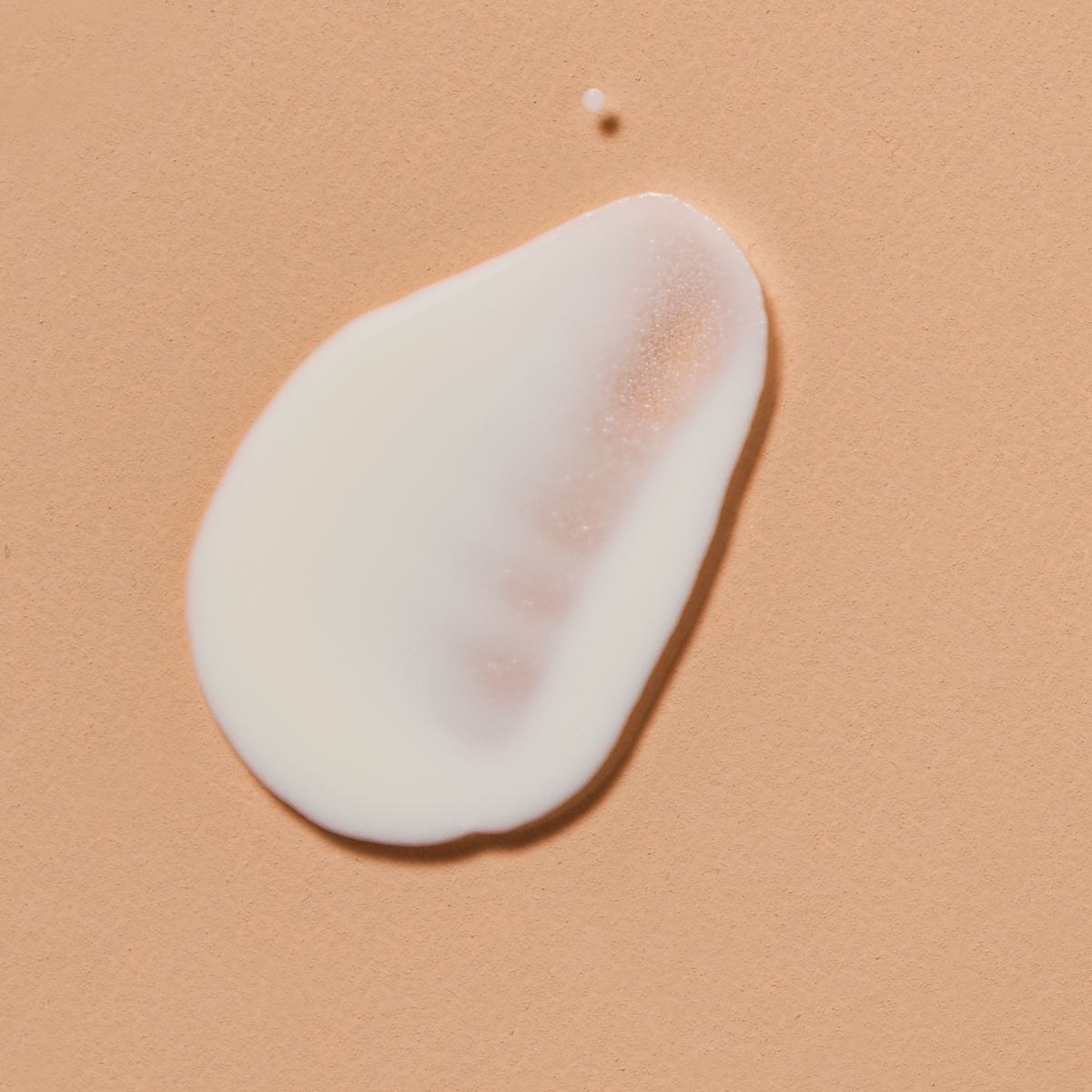 Noisette de crème blanche Colorescience No-Show Mineral Sunscreen FPS 50 étalée sur fond pêche