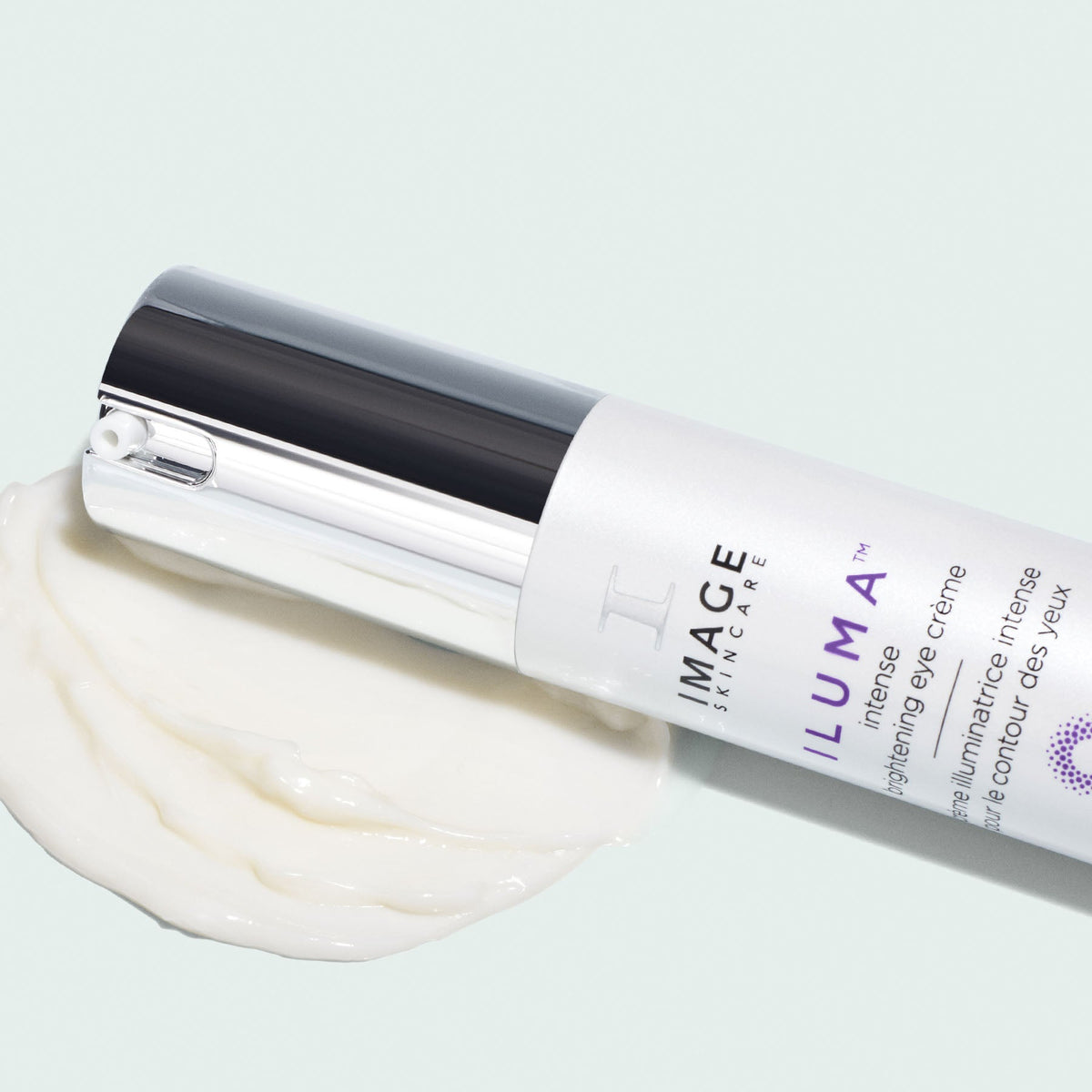Flacon ILUMA crème illuminatrice contour des yeux d’Image Skincare couché sur une trace de crème blanche