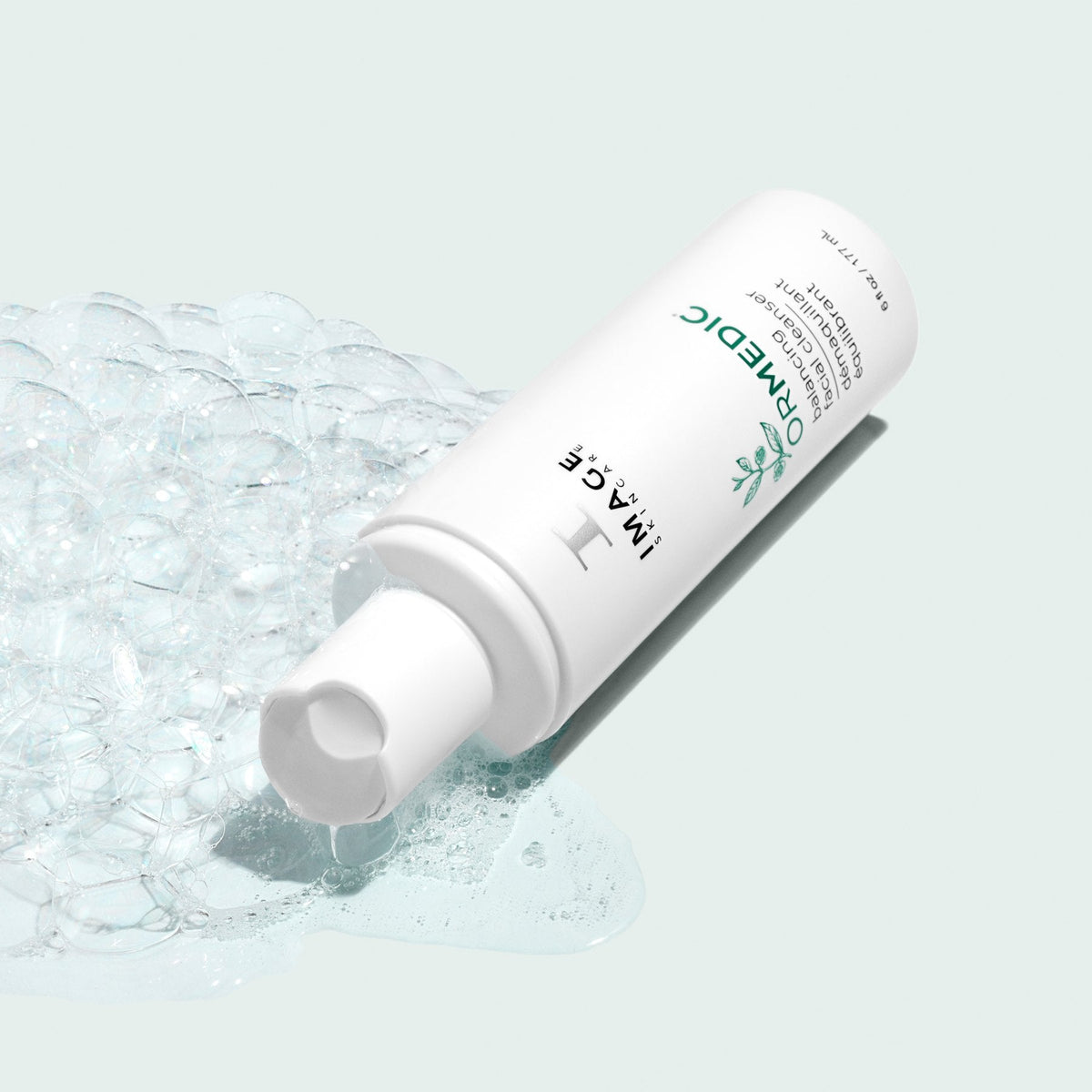 Flacon ORMEDIC nettoyant facial équilibrant d’Image Skincare couché dans une mousse transparente, fond vert pâle