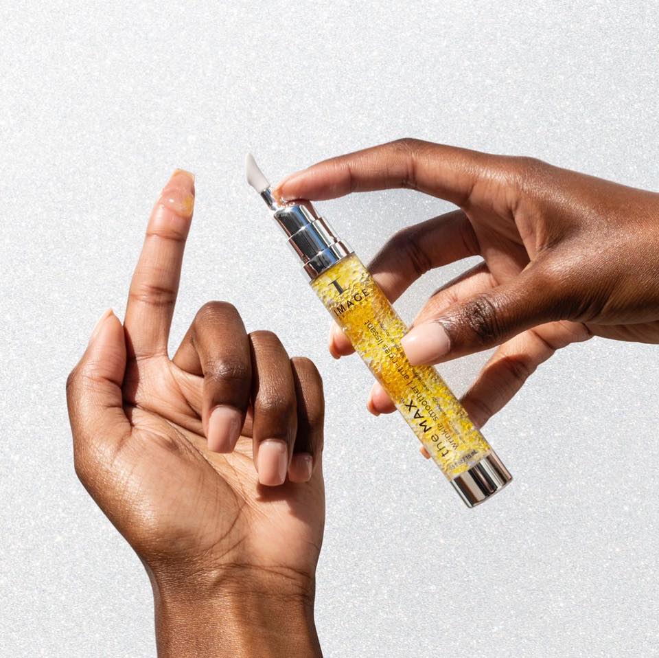 Une main tient le tube transparent the MAX anti-rides lissant d’Image Skincare au gel doré, une goutte sur l’index de l’autre