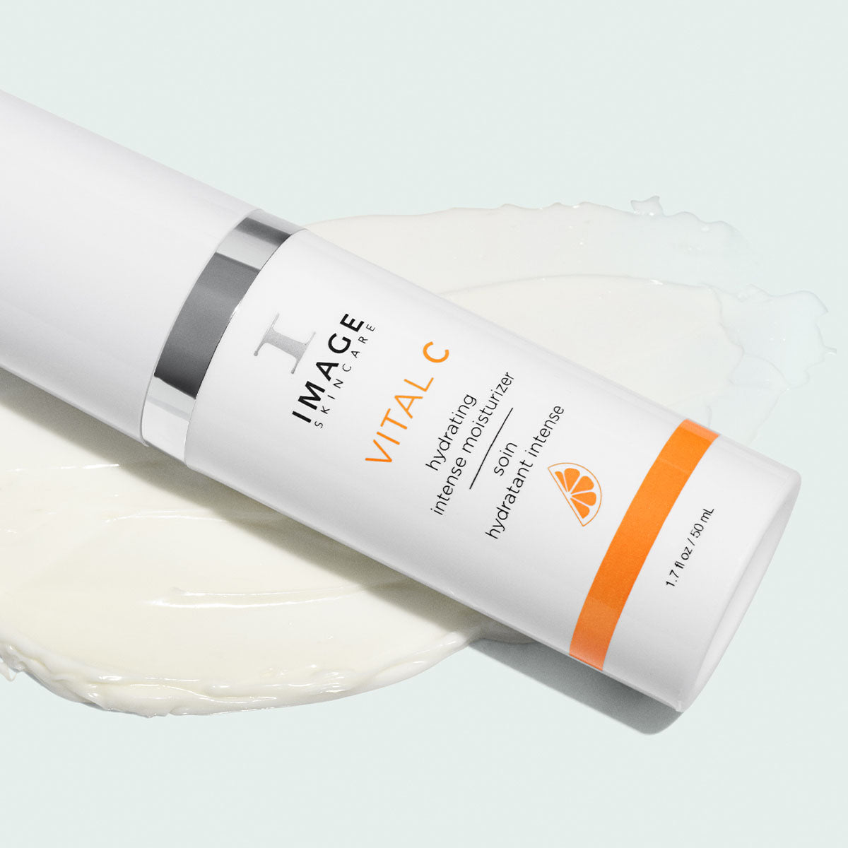 Flacon blanc VITAL C soin hydratant intense d’Image Skincare couché sur une traînée de crème blanche, fond vert pâle