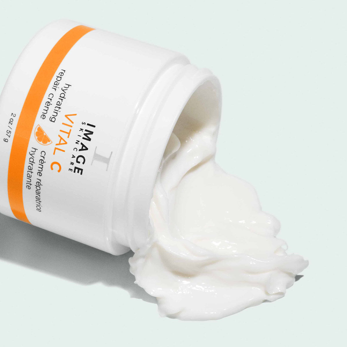 Pot blanc et orange ouvert et couché, crème réparatrice hydratante VITAL C d’Image Skincare, crème blanche qui s’en échappe
