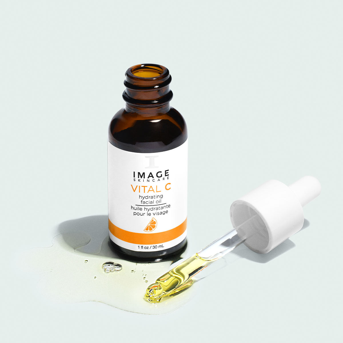 Flacon ambré ouvert, huile hydratante pour le visage VITAL C d’Image Skincare, compte-gouttes posé dans une flaque d’huile