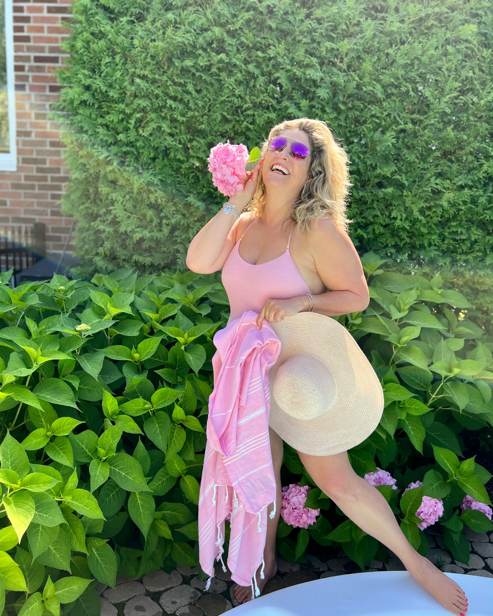 A woman in a straw hat holding a pink Luna towel in a garden