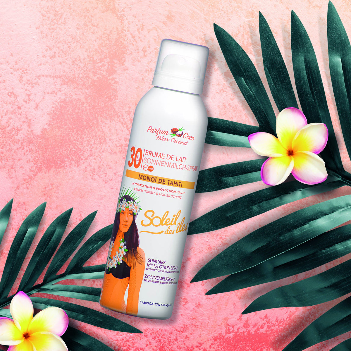 Aérosol Soleil des Îles, Brume de lait coco FPS 30 au Monoï de Tahiti, sur fond rose avec palmes et fleurs tropicales