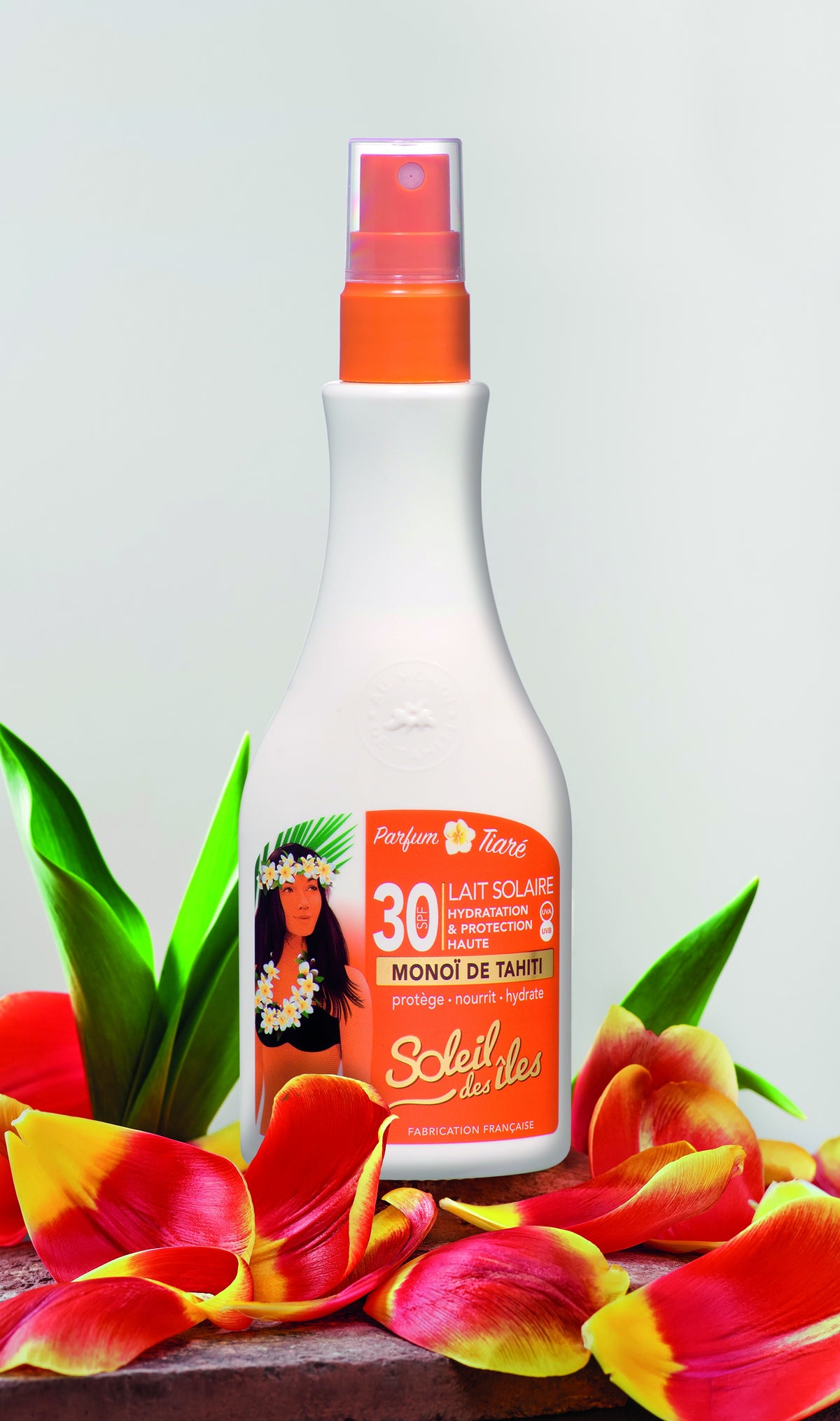 Soleil des Îles SPF 30 sun milk with Monoï de Tahiti bottle among red and yellow petals and green leaves